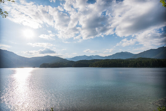 Sunny beach at Eibsee lake with turquoise water and green forest under bright sun at Zugspitze Mountain
