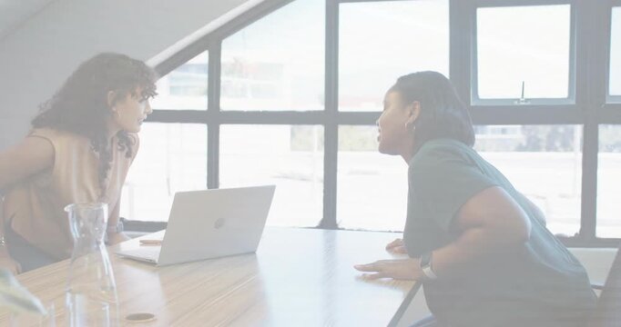 Two pros leaning at business table, checking laptop then standing shaking hands, sparking deal icon
