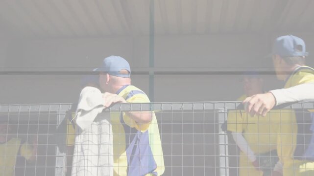 Team members leaning on railing reacting to off-field play waving towel pointing shielding eyes