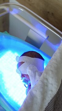 High bilirubin treatment for a newborn child. Tiny baby lies on a ultraviolet lamp in a crib covered with blanket. Top view. Vertical video