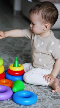 One year old toddler disassembling the toy pyramids. Little baby boy plays on the floor at home. High angle view. Vertical video