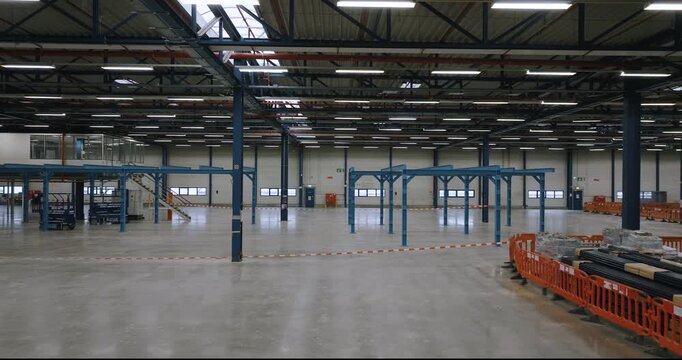 Interior view of a large empty industrial warehouse with blue steel support beams and overhead lighting