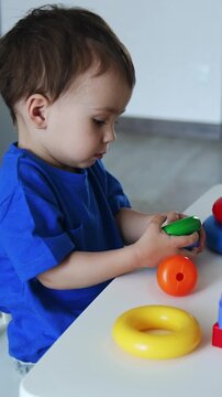 Small toddler boy turning colorful toys in hands. Lovely kid sits peacefully at desk in his room. Vertical video