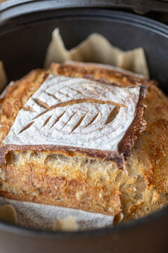 Artisan sourdough loaf with decorative scoring in a cast iron pot