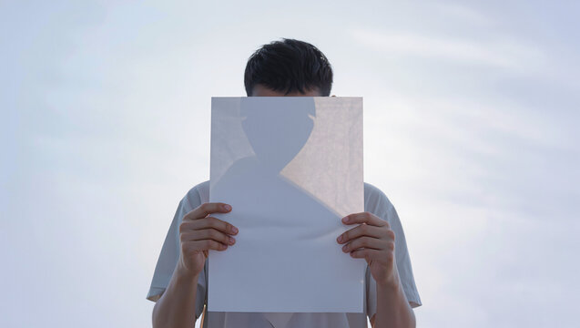 Identity concealed: man holding silhouette cutout against bright sky