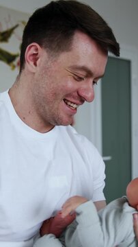 Caucasian man in white t-shirt waving his newborn baby. Happy father dandling his little son in maternity hospital. Vertical video