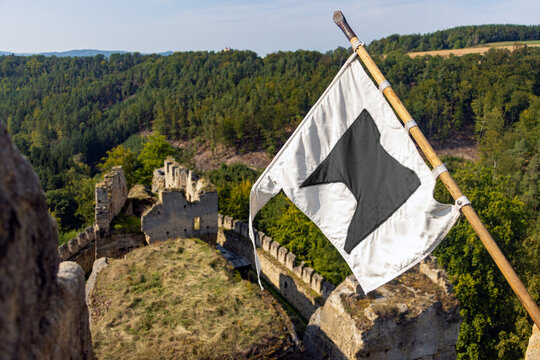 A white flag with a distinctive black emblem hangs on a wooden flagpole attached to a castle tower overlooking at castle