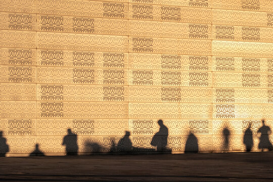 Urban architecture wall with pattern and texture captures shadow silhouette of people as evening crowd forms an abstract street scene in light