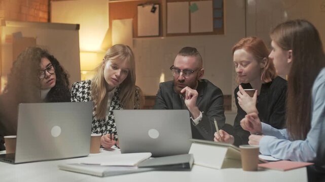 Professional business team reviewing a tablet and discussing project details during an office meeting. Women and men, coworkers, colleagues or employees sharing ideas, checking information, making