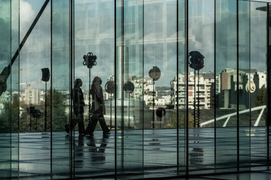 Reflections on a glass facade reveal silhouettes of pedestrians in corporate business finance architecture at La Defense Paris within a modern office district scene