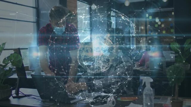 Vertical video: Standing man pointing at laptop seated dev typing initiating holo globe for IT demo