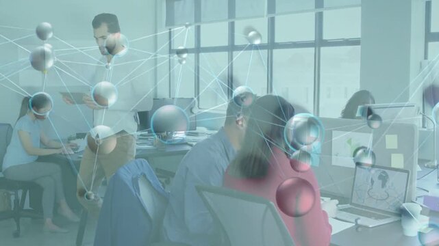 Standing man tapping tablet causing molecular overlay while team leaning at laptop for tech review