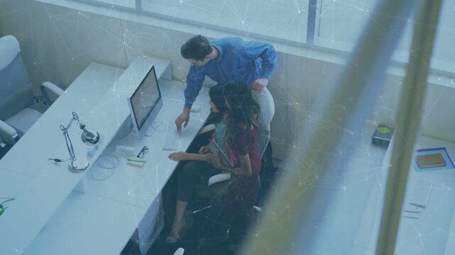 Vertical video: Man walking up and leaning behind woman using mouse to show monitor for business