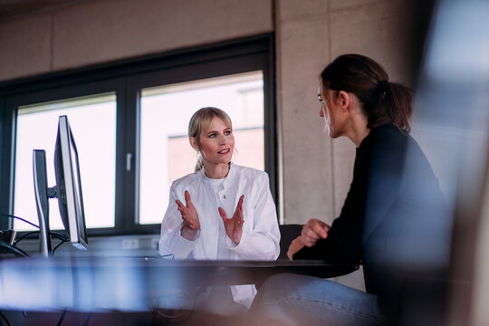 Female doctor discussing with patient sitting at computer desk in hospital