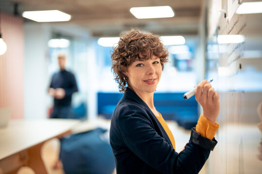 Smiling young businesswoman planning and writing on whiteboard in office