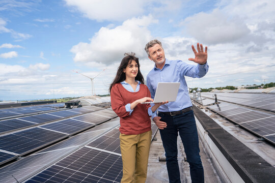 Mature businessman discussing with young colleague holding laptop and standing on rooftop