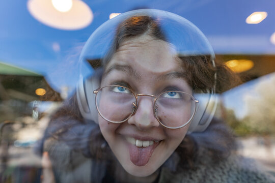 Smiling girl with headphones and glasses at urban cafe window