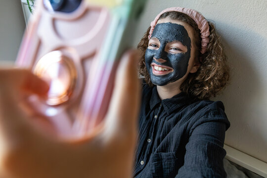 Smiling girl with facial mask taking a selfie at home