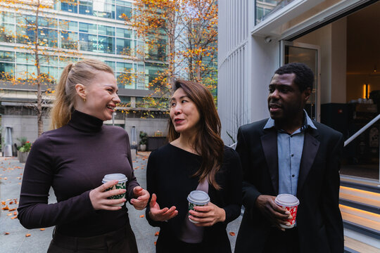 Business colleagues walking outdoors discussing teamwork with coffee
