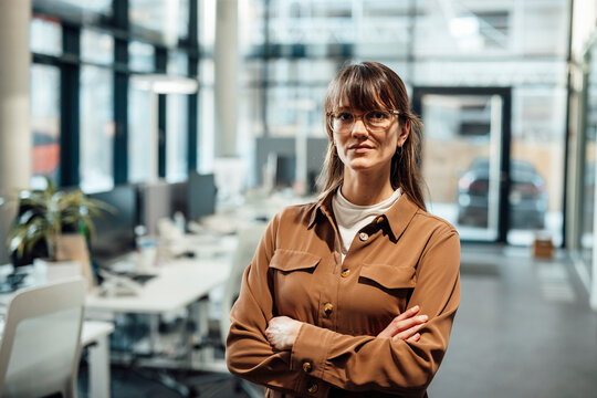 Businesswoman in modern office with arms crossed looking confident