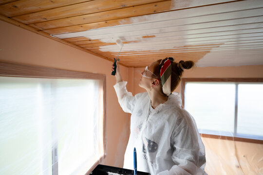Homeowner painting wooden ceiling white with roller indoors