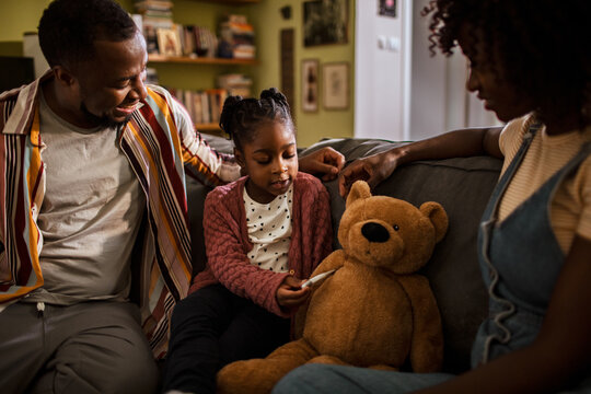 Parents supporting daughter playing doctor with teddy at home