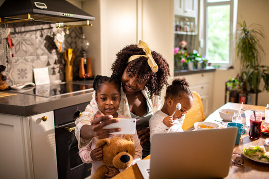Mother with two daughters taking selfie at breakfast in home kitchen