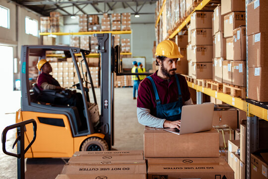 Warehouse workers using laptop and forklift in distribution center
