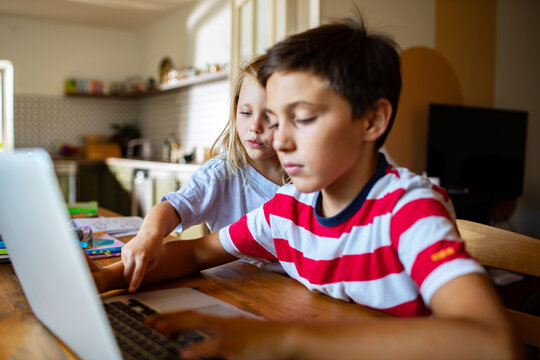 Siblings studying on a laptop at a home kitchen table