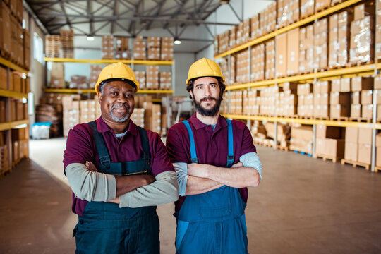 Two warehouse workers in hard hats standing with arms crossed in distribution center