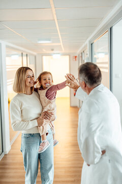 Doctor giving high five to child with mother in hospital hallway