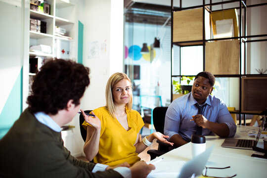 Coworkers discussing project with woman shrugging in office