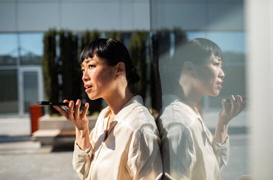 Businesswoman using smartphone voice assistant outside office building