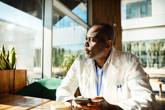 Doctor using smartphone in hospital cafe during coffee break