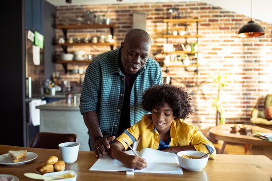 Grandfather helping grandson with homework at kitchen table