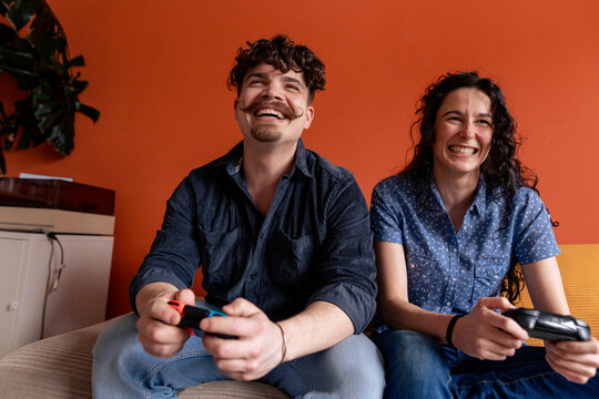 Happy couple playing video game sitting on sofa at home