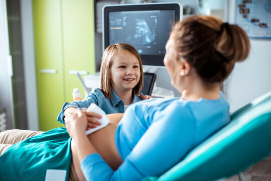 Smiling child with pregnant mother during ultrasound exam in clinic