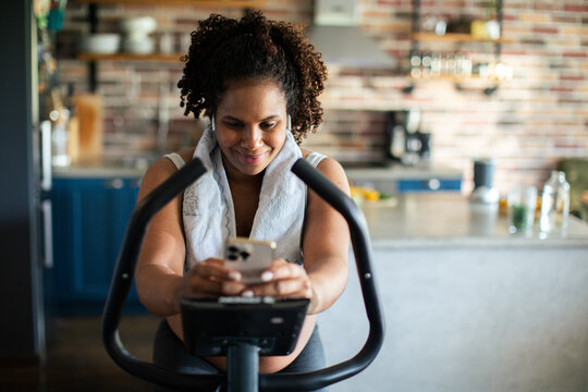 Woman on stationary bike using smartphone in home kitchen