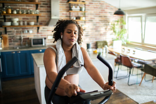 Pregnant woman cycling on stationary bike at home kitchen