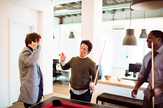 Coworkers playing pool in modern office break room