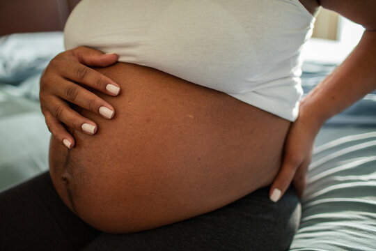 Pregnant woman cradling belly at home