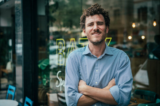 Happy businessman with arms crossed standing outside cafe