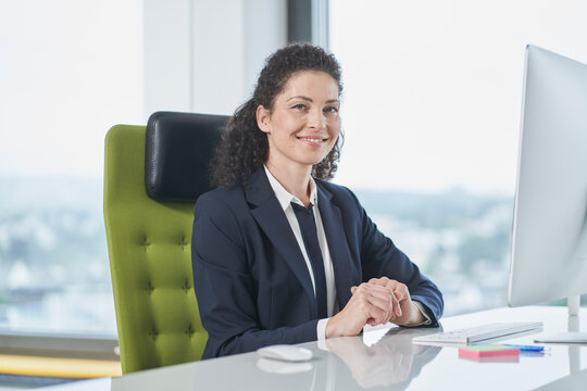Happy mature businesswoman sitting with computer at desk in office
