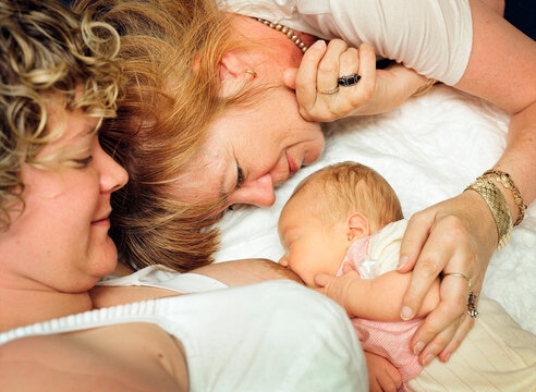 Mother breastfeeding baby with grandmother looking on indoors