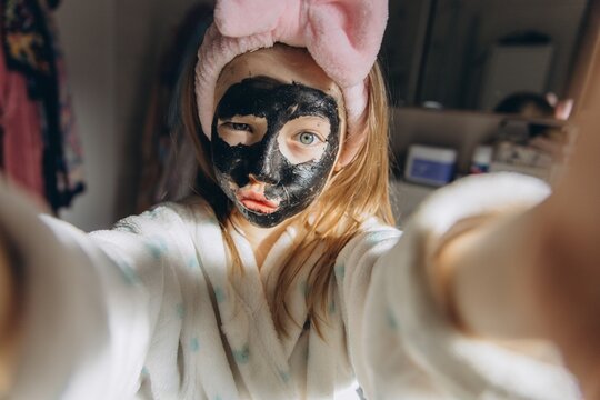 Child applying facial mask taking playful selfie in bathroom