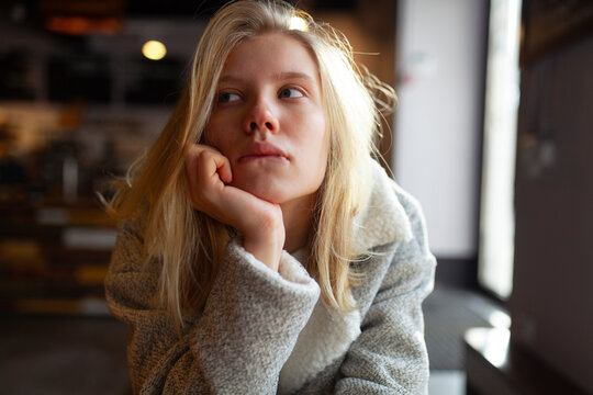 Young woman sitting at wooden table in cozy cafe with thoughtful expression