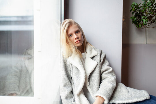 Blonde woman in coat sitting by window at cafe looking relaxed