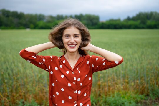 Woman with curly hair in red blouse smiling in wheat field outdoors
