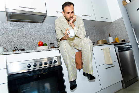 Tired man sitting on kitchen counter holding a coffee mug