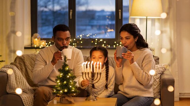 Lighting parents in light sweaters using taper lighting menorah on couch, celebrating holiday